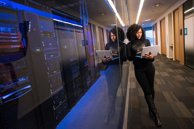 Woman holding laptop beside glass wall