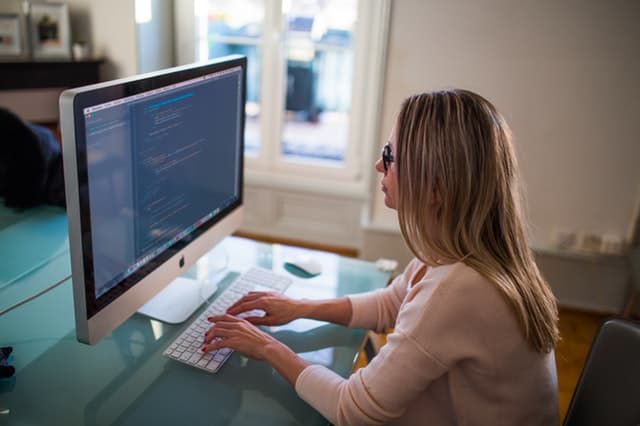 Seated woman typing on silver Imac